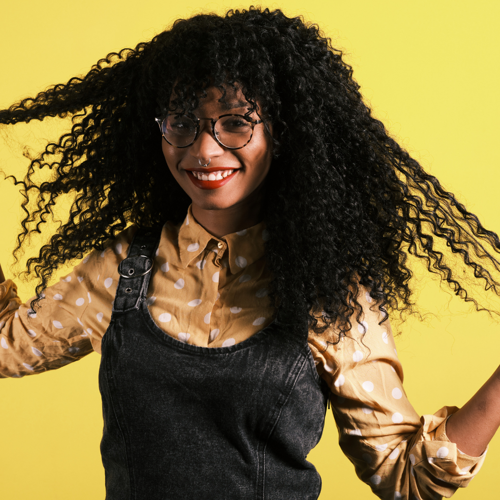 black girl with long curly hair wearing red lipstick portrait in front of yellow background 