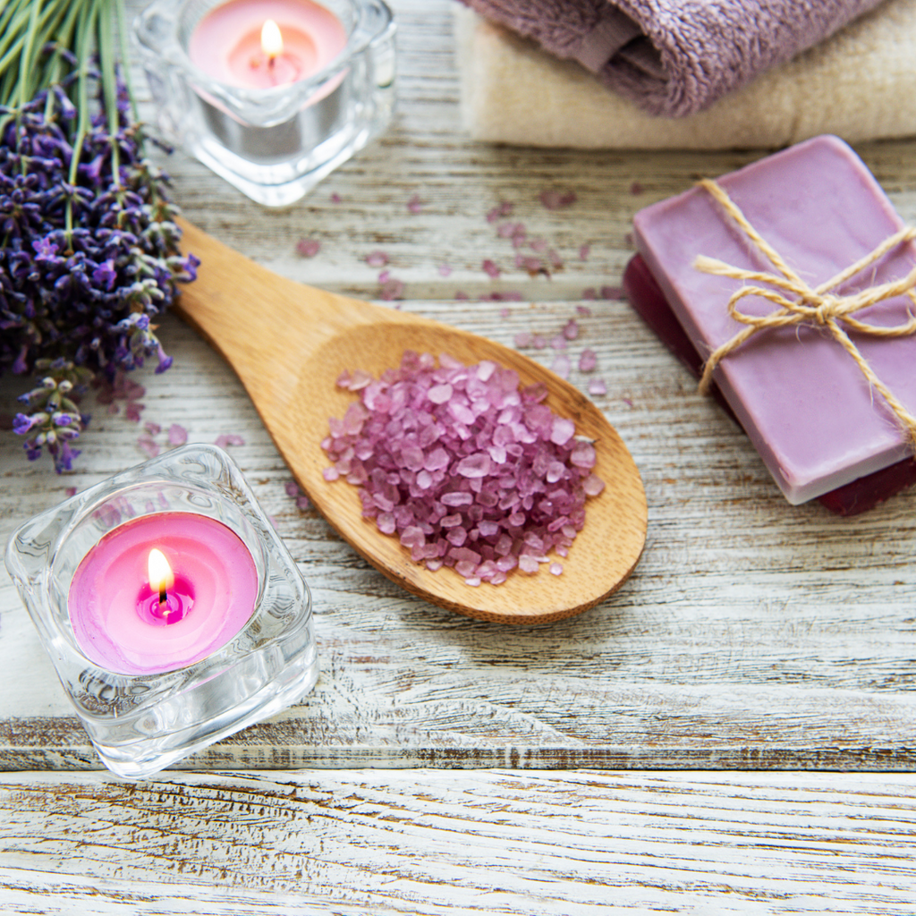 Flat lay display of candle, spoon with purple salts and a lavender bar soap wrapped with twine. 
