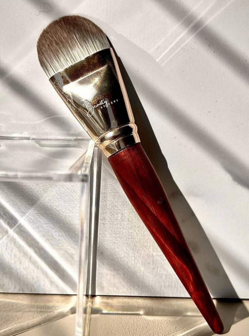 Makeup brush with red handle and silver ferrule on a reflective surface