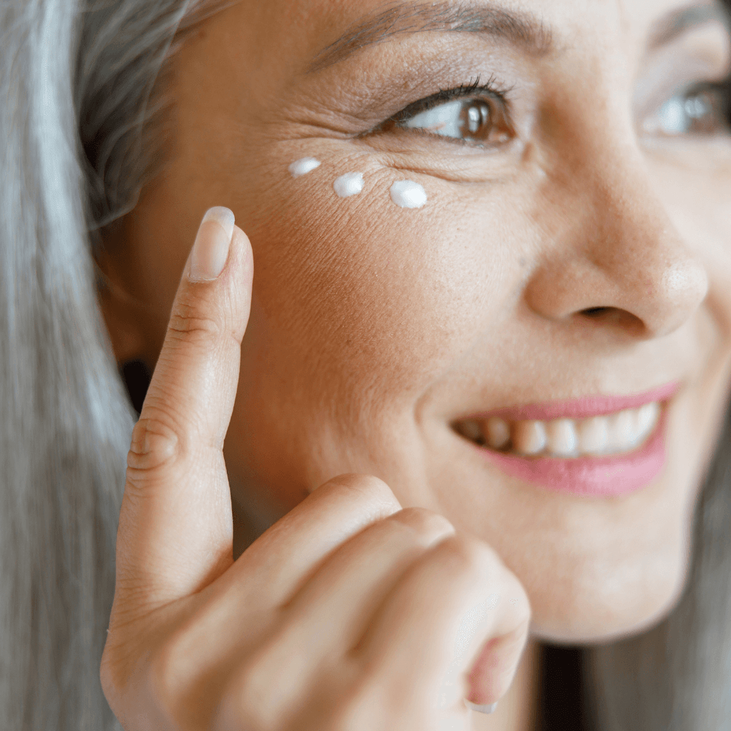 mature white woman smiling while pointing to cream under eye 