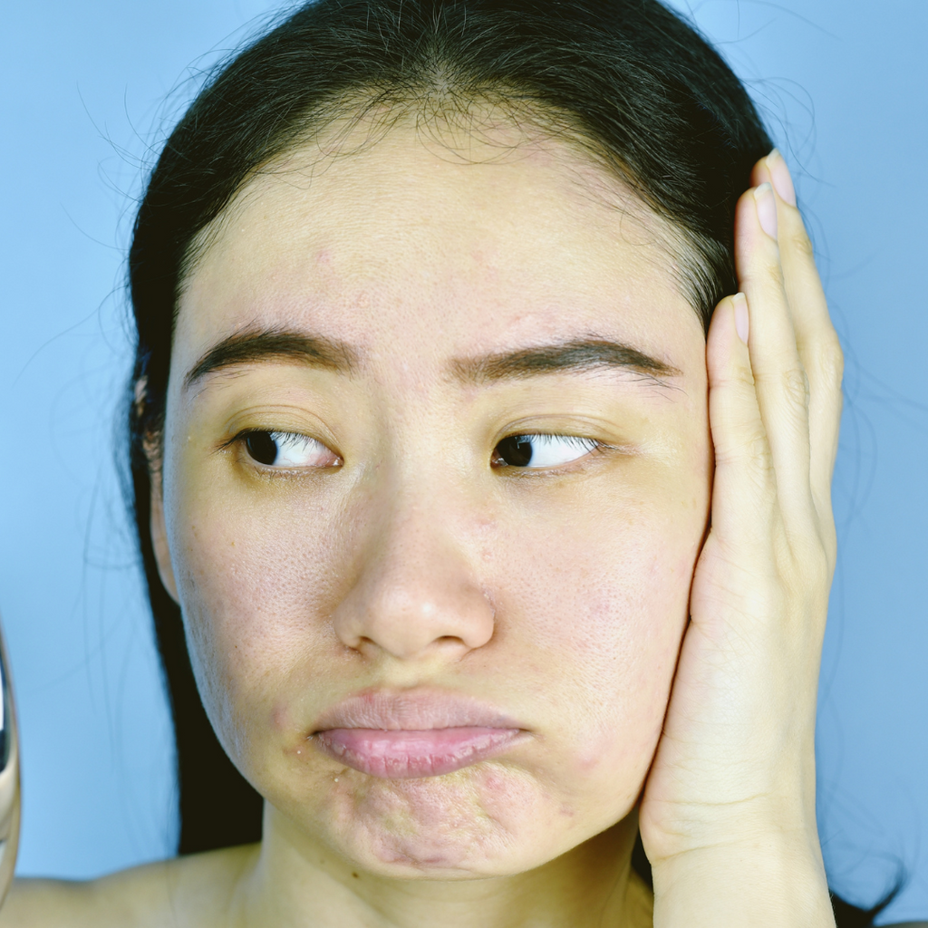 Asian woman with sad face covering left ear with left hand on blue background