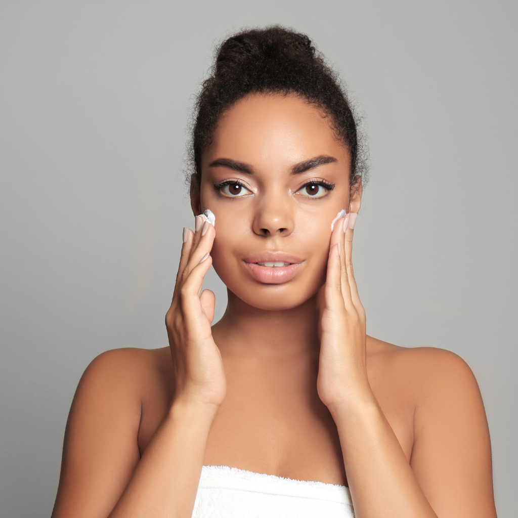 African American woman wrapped in white towel portrait applying cream to both of her cheeks 