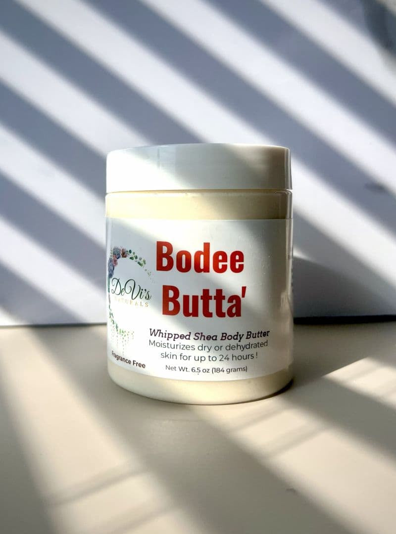 Bodee Butta whipped shea body butter jar on a light surface with striped background