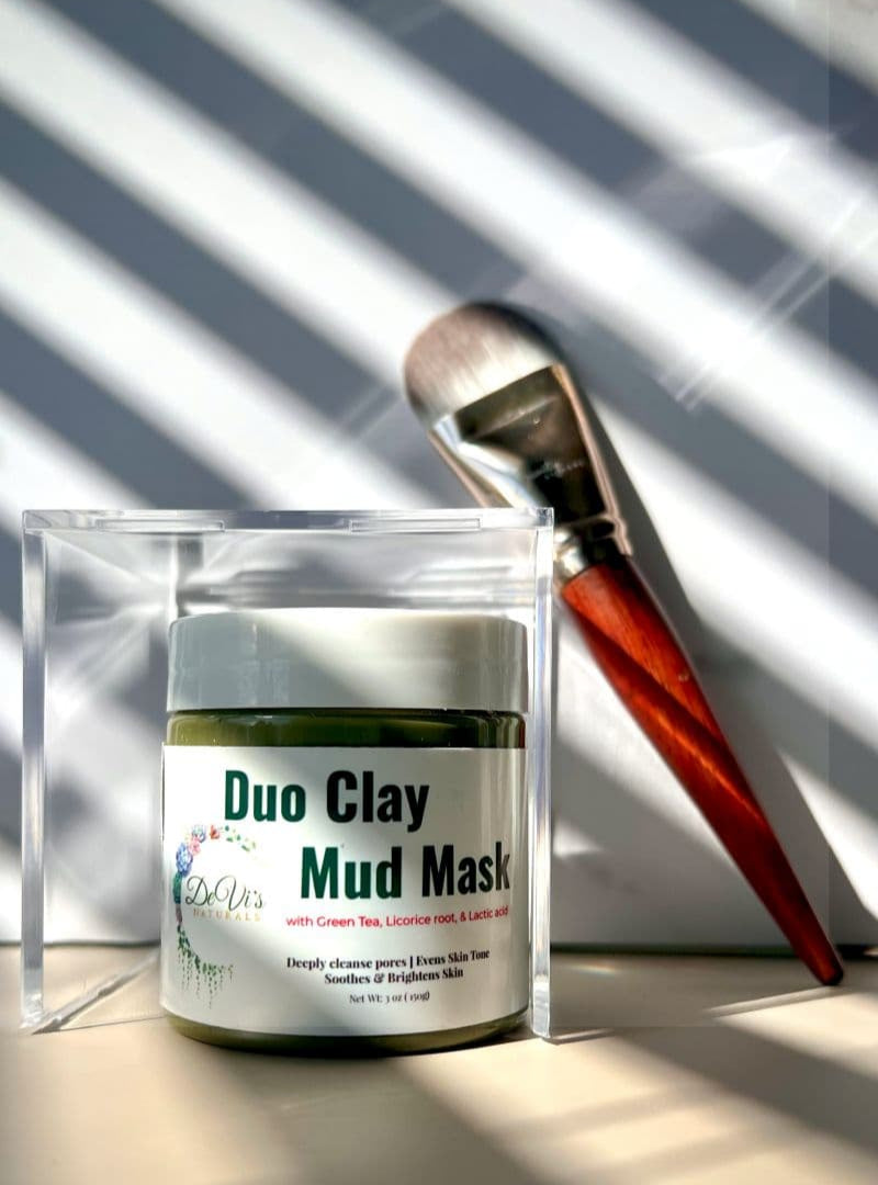 Duo Clay Mud Mask jar with a brush on a striped background