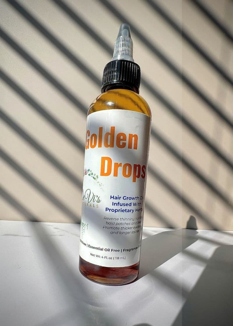 Bottle of Golden Drops hair growth product on a reflective surface with a striped background