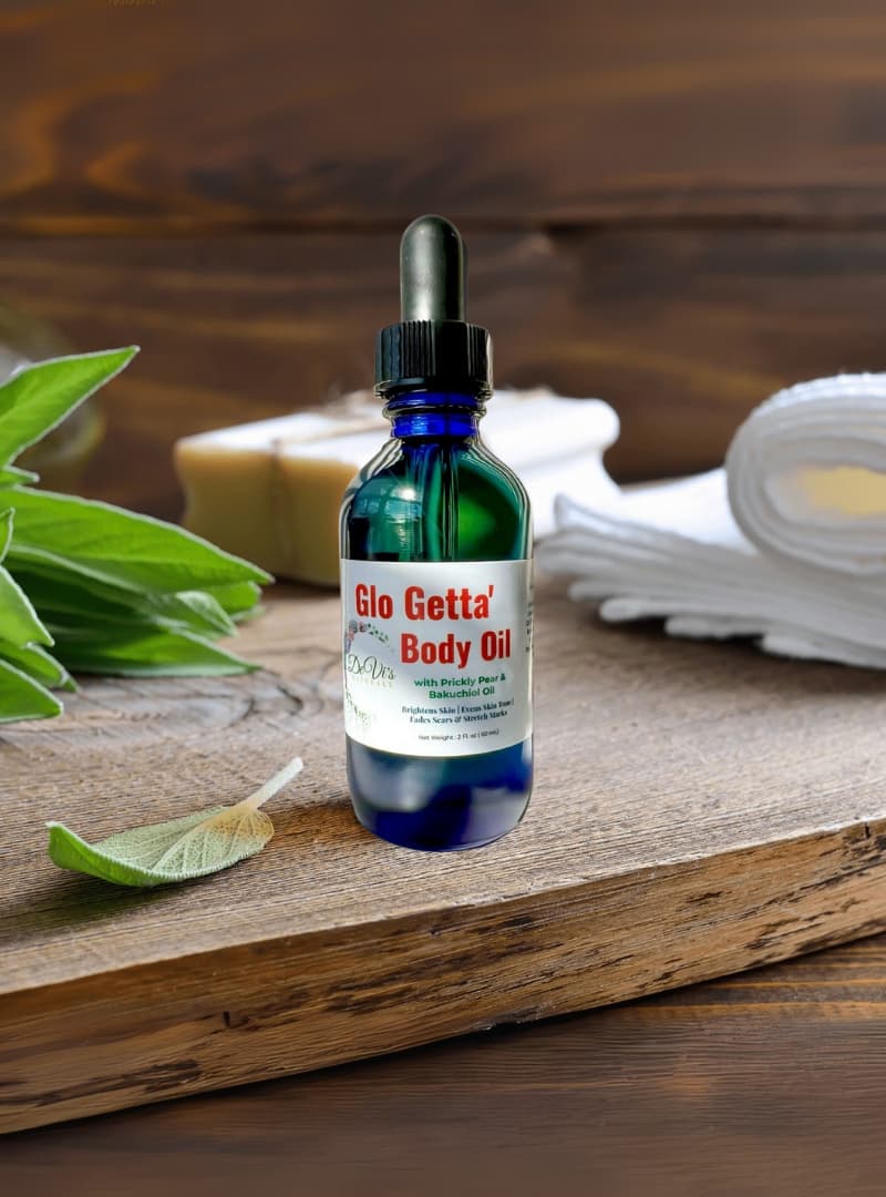 Bottle of Glo Getta Body Oil on a wooden surface with green leaves and a white cloth in the background.