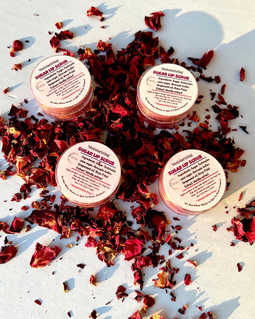 Four containers of sugar lip scrub surrounded by dried red flowers on a white surface.